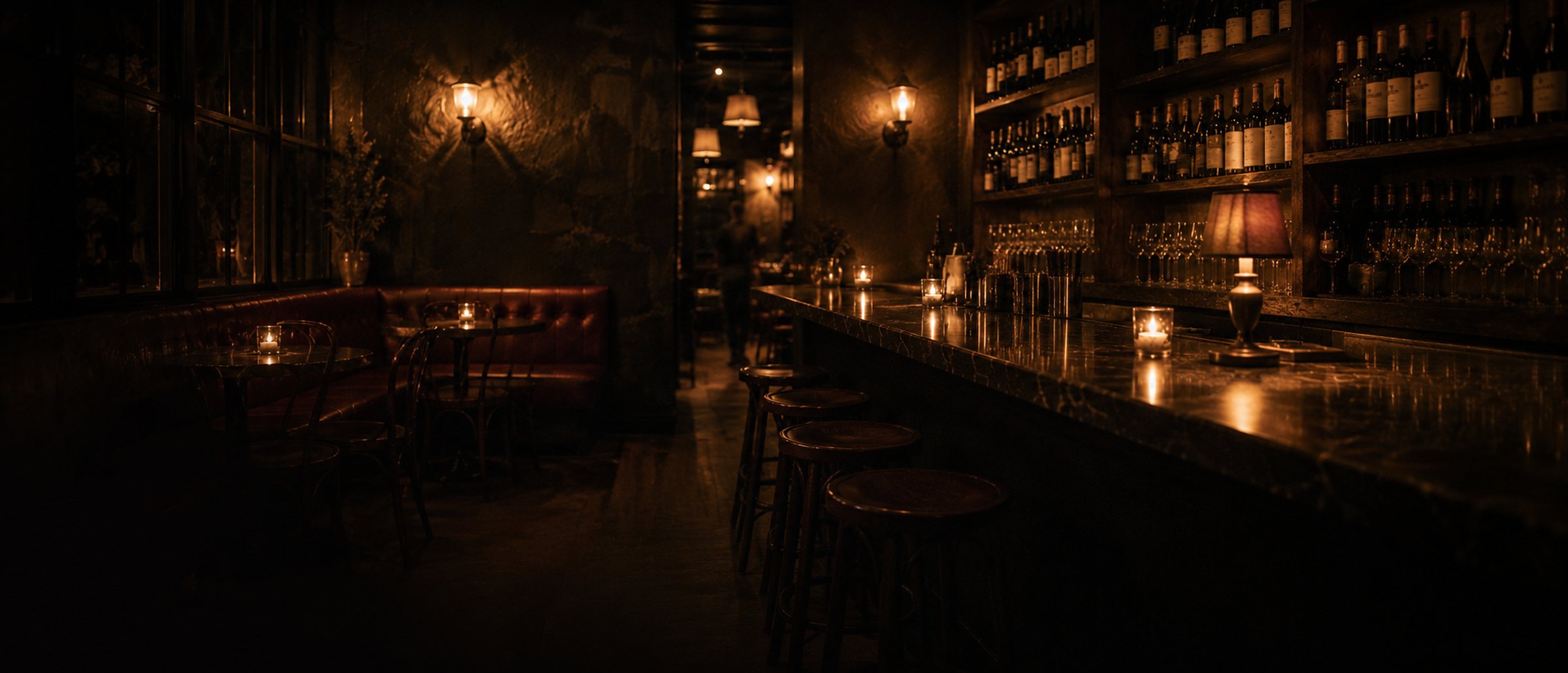 The wine bar at candlelight, marble counter and low lamps, the corner booth glowing.