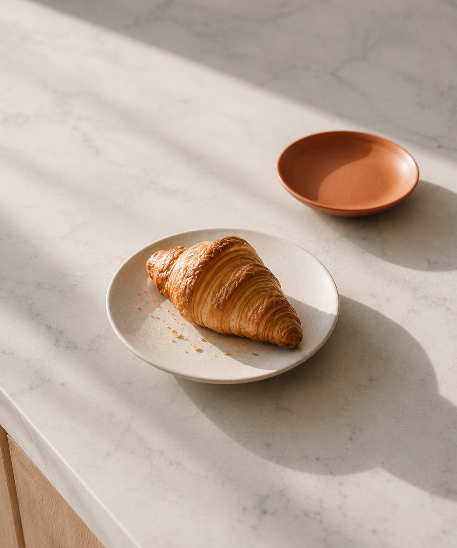 A single croissant on a ceramic plate on a marble counter.