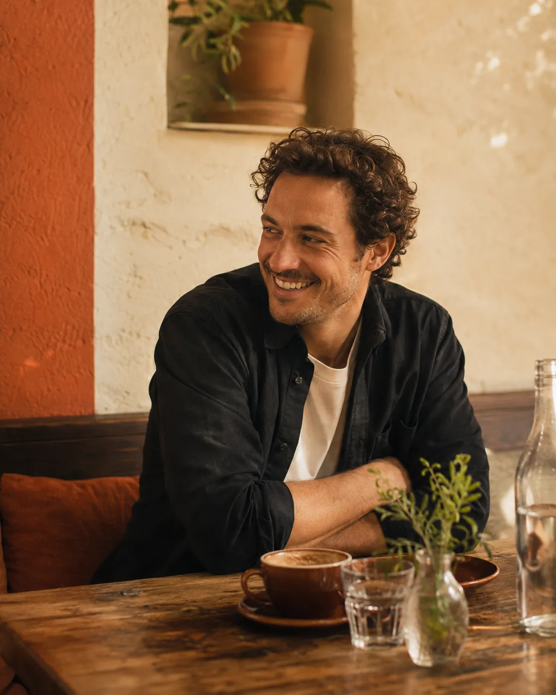 Cafe founder relaxed at a timber table with a flat white, warm side light and terracotta tones.