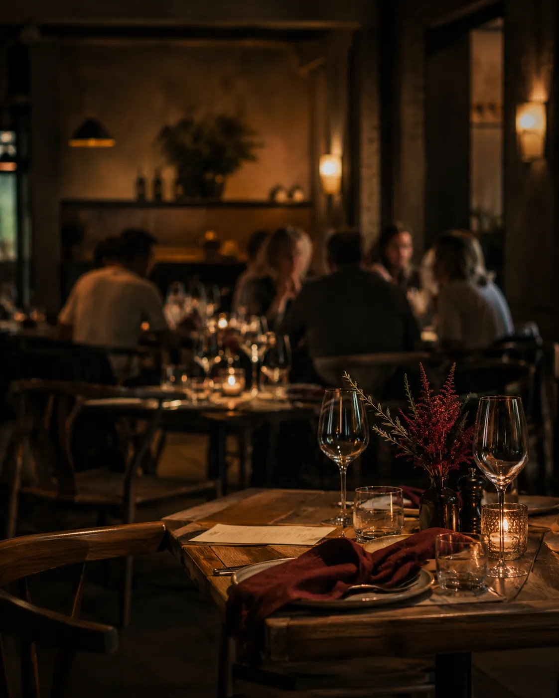 Candlelit dining room at service, tables set with glasses and napkins, guests in the background
