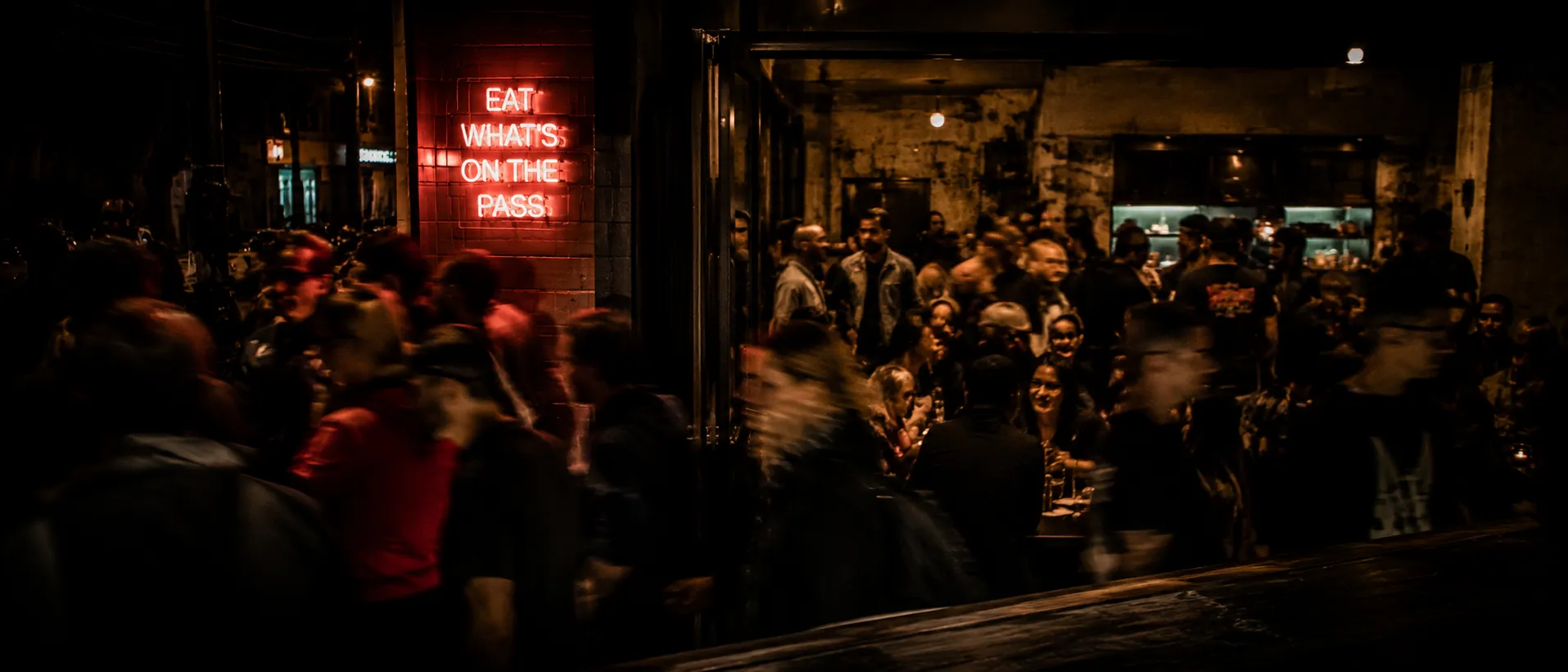 Restaurant room mid-service, communal table, hands reaching across plates, loud and real